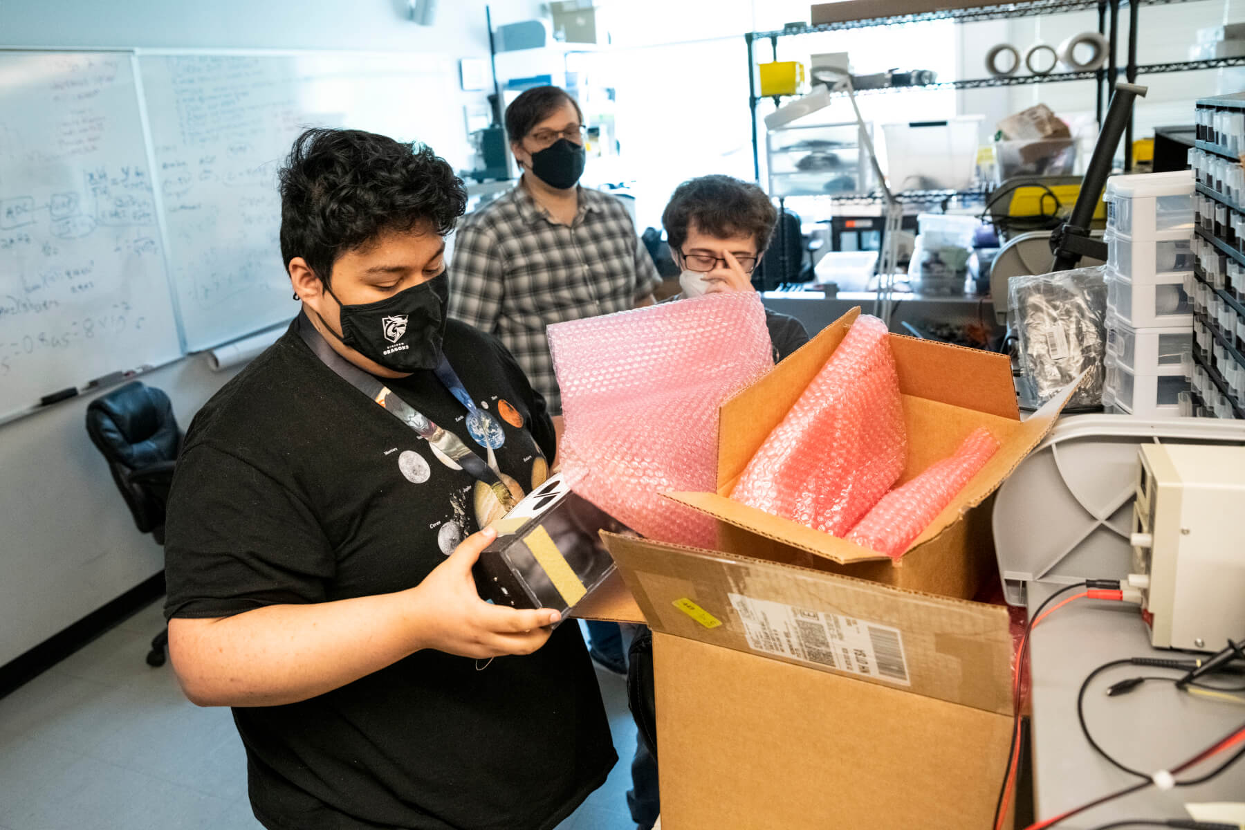 Student in lab pulls a small black box from a larger cardboard box.