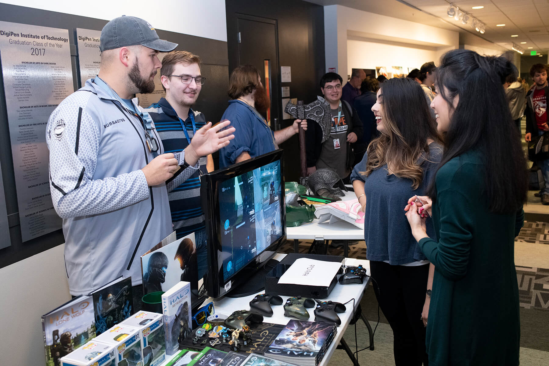 Students and staff talk while standing around a table filled with Halo memorabilia.