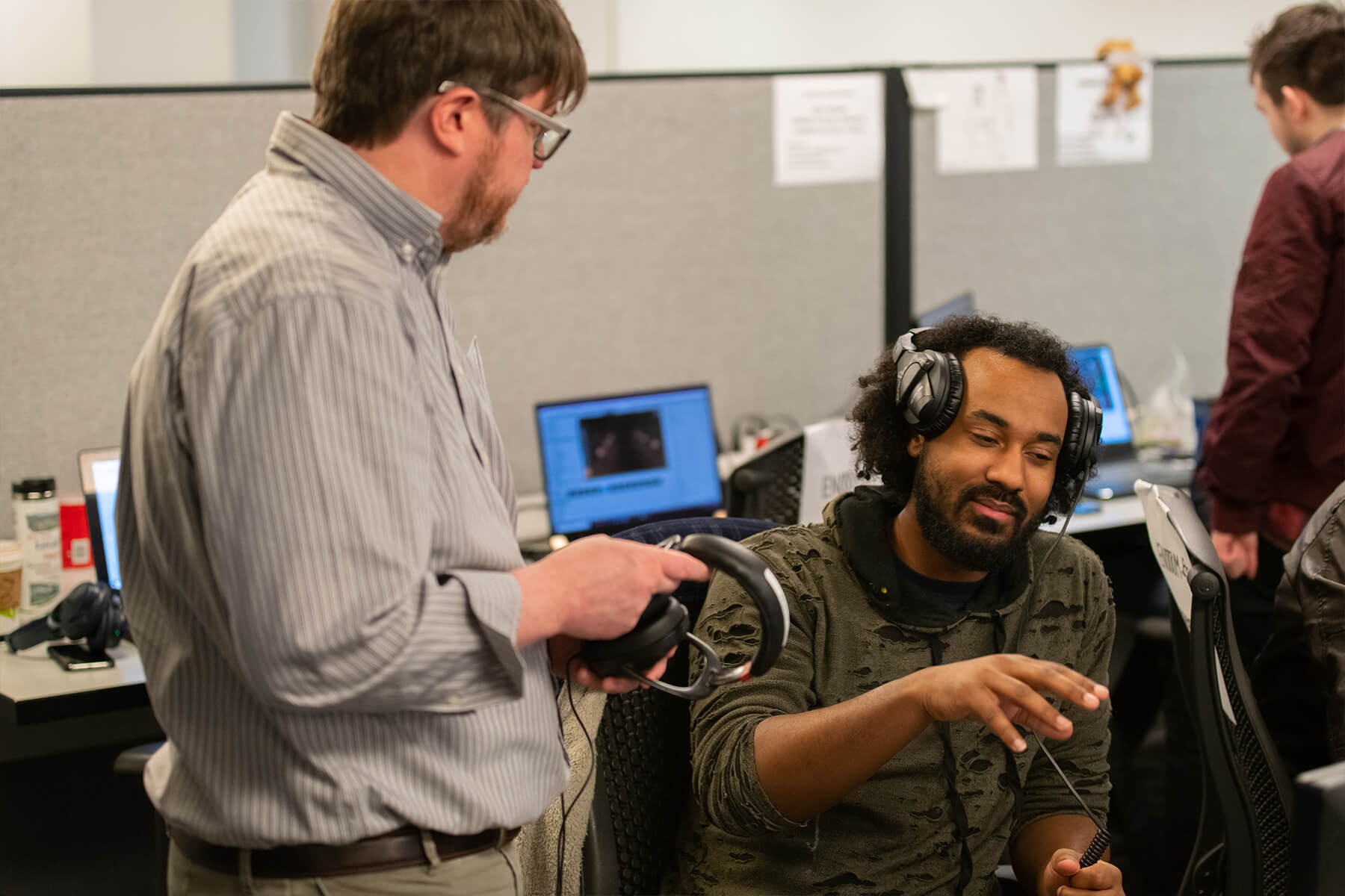 A professor takes his headphones off to chat with a student, also wearing headphones, about their work.