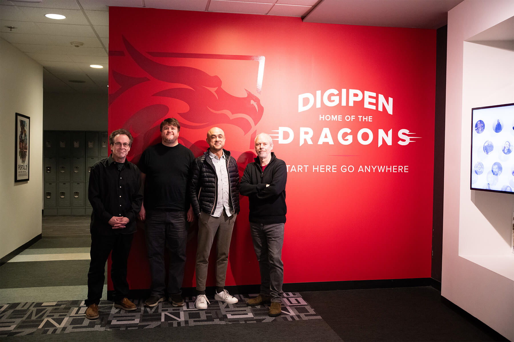 Bruce Stark, Greg Dixon, Tacket Brown, and Lawrence Schwedler stand in front of a Dragon decal on DigiPen’s campus.
