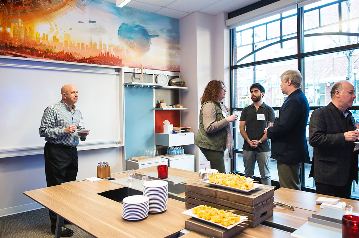 community members converse with DigiPen staff in a conference room featuring student art wallpaper at the Redmond Marriott