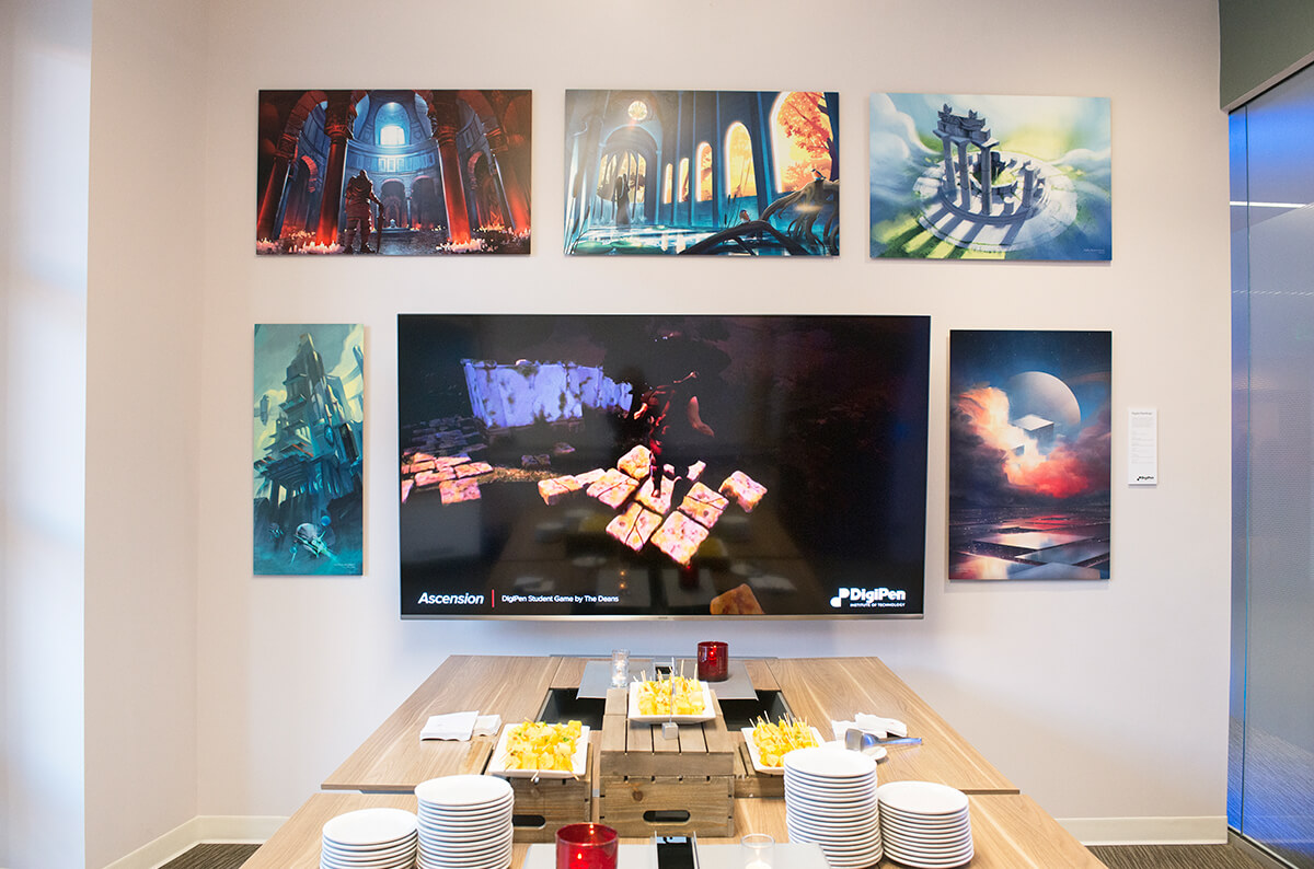 5 large pieces of DigiPen student artwork surround a large flat-screen tv playing a student game trailer in a conference room at the Redmond Marriott