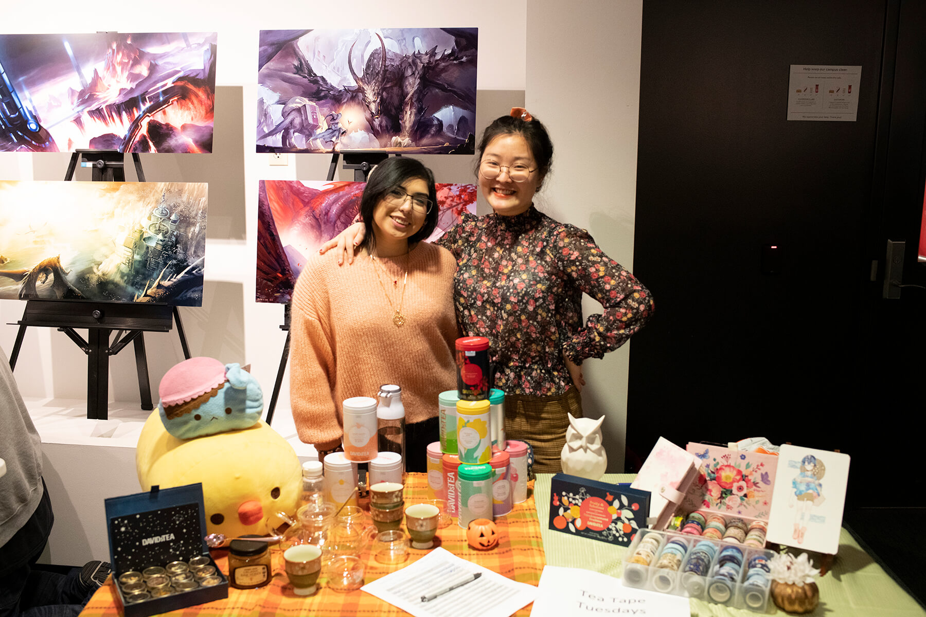 Two students stand behind a table arranged with teas and knickknacks.