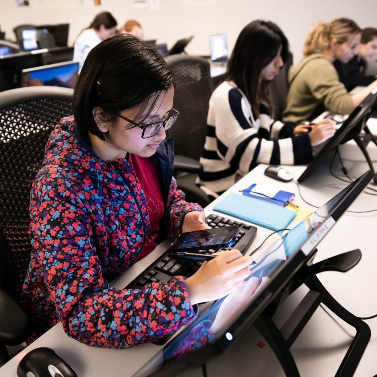 A student in a lab classroom draws on a tablet using a stylus.