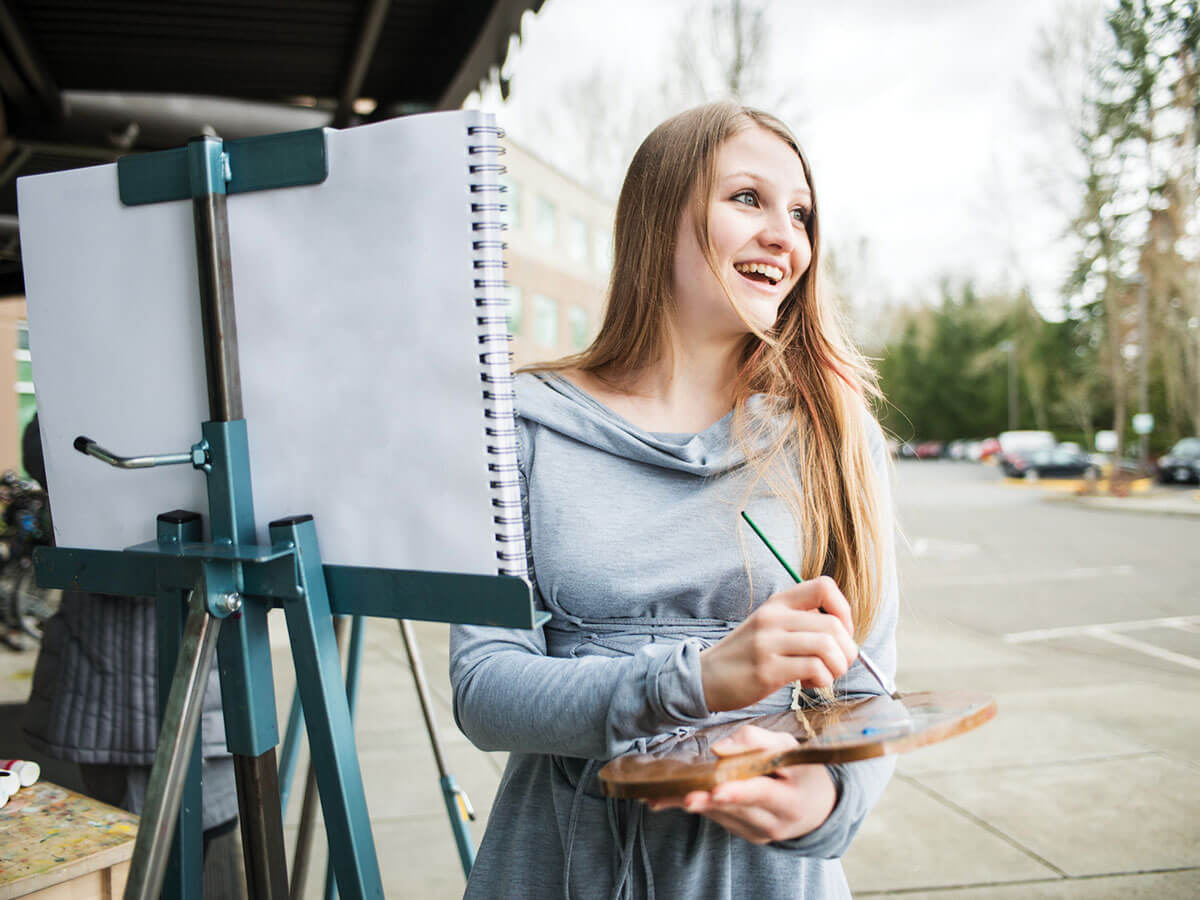 A BFA student stands in front of an easel outside of a DigiPen building