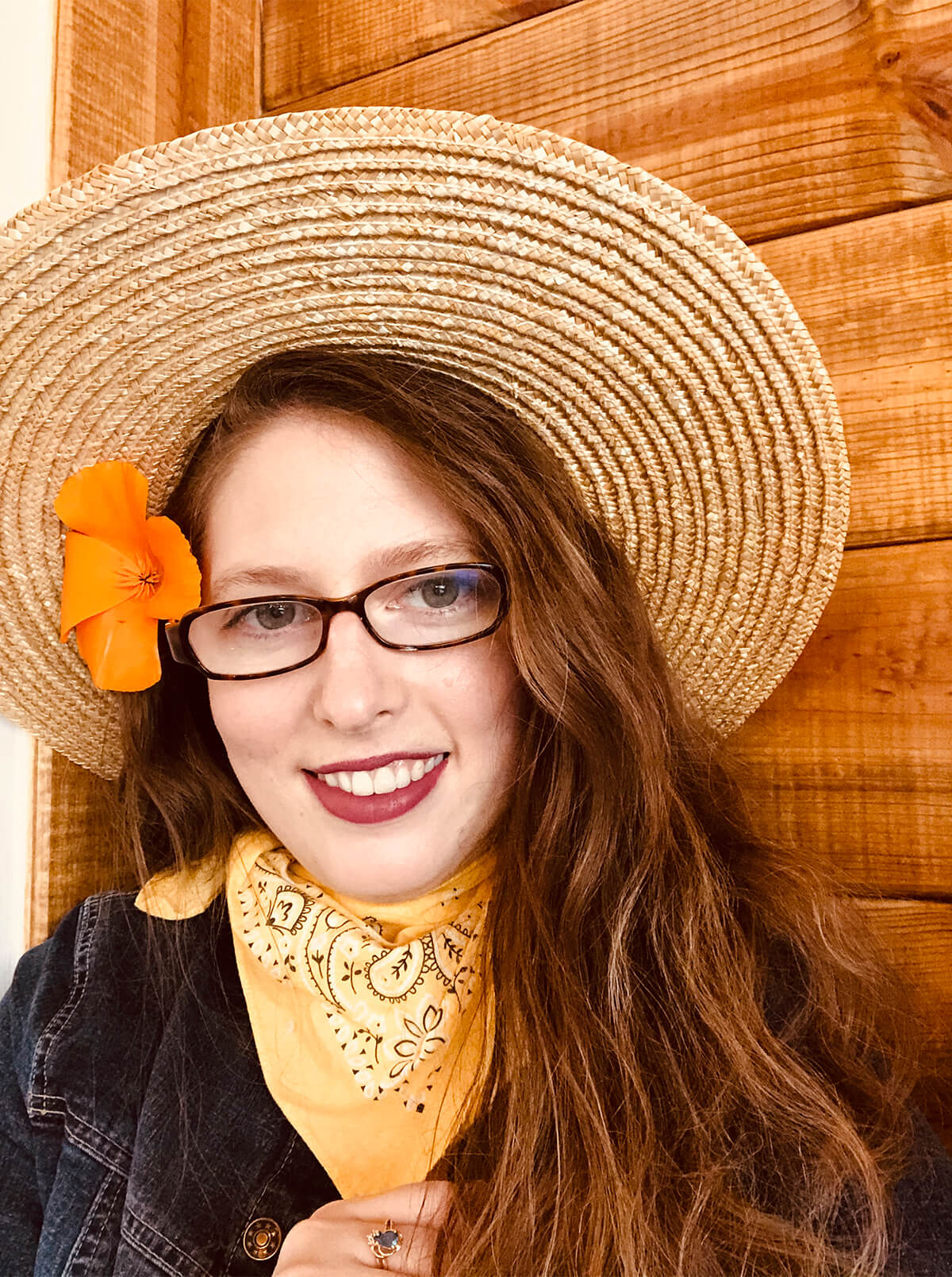 DigiPen MFA graduate Hannah Patten smiles in a straw hat with an orange flower in her hair.