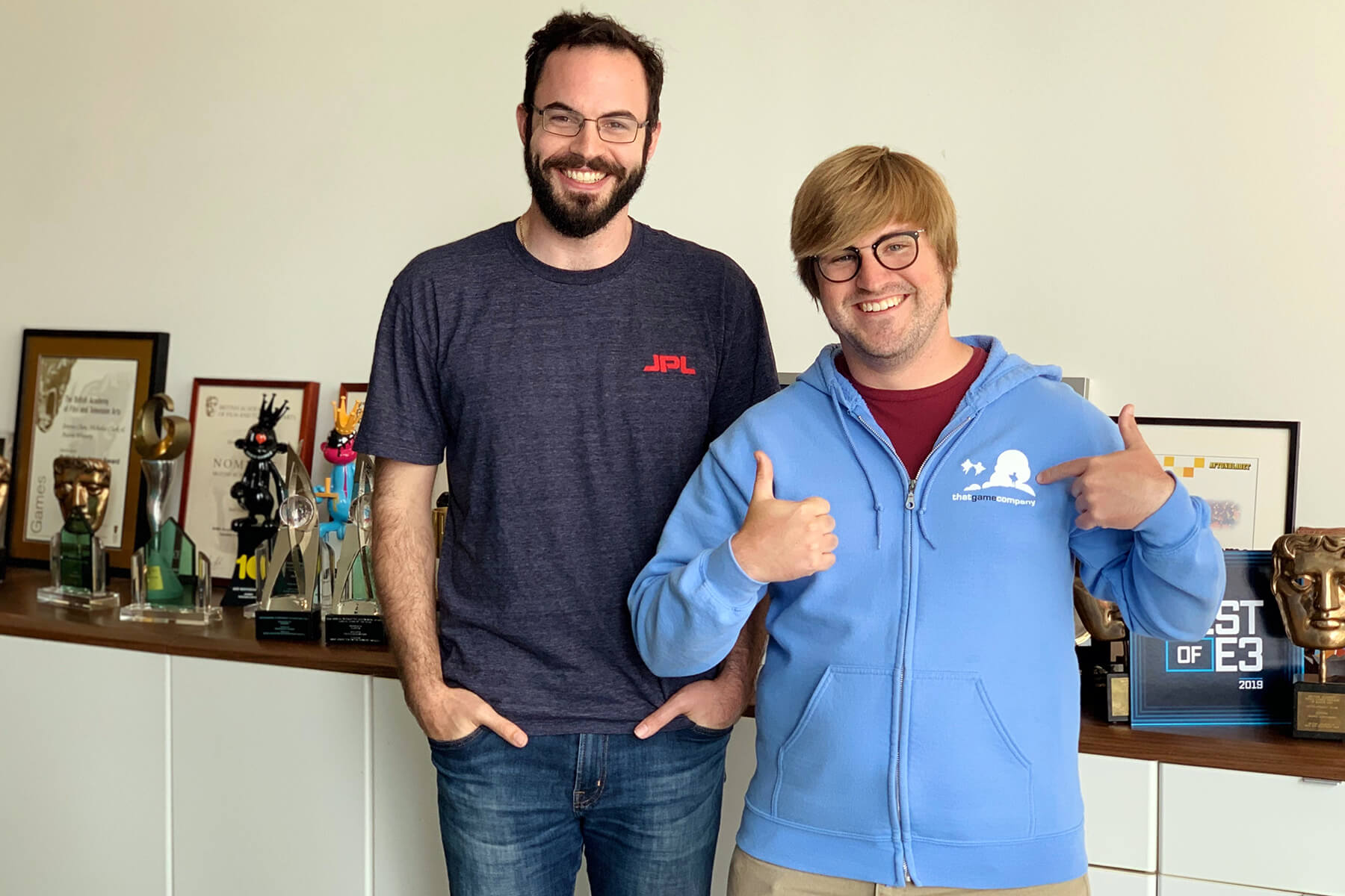 John Hughes and Kyle Holdwick pose in thatgamecompany's offices, surrounded by awards.