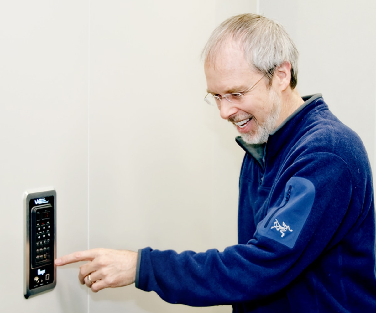 Lawrence Schwedler pointing to a wall-mounted control box in a new DigiPen sound lab practice room