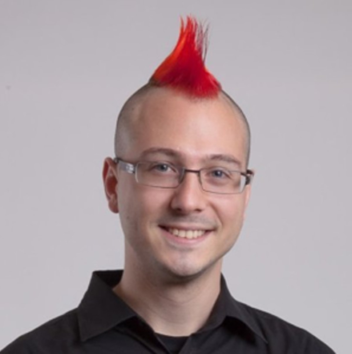 Headshot of a smiling Mikhail Davidof, who has a red mohawk hairstyle