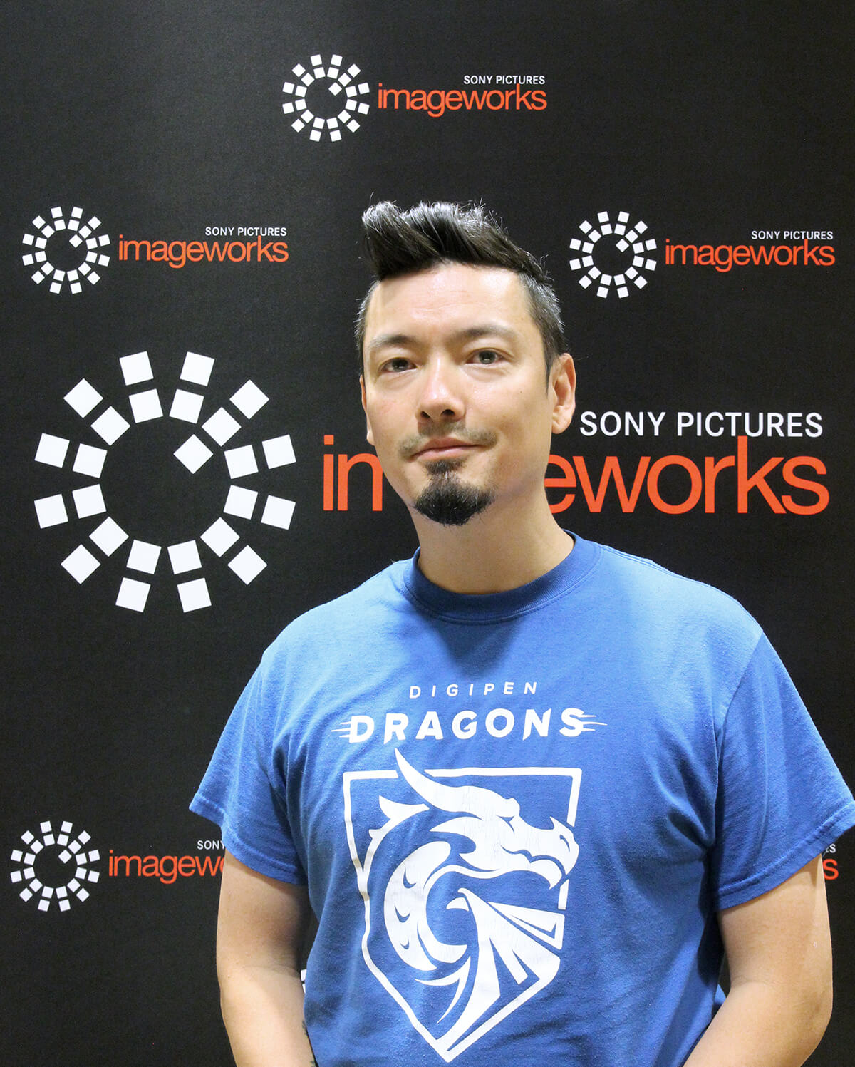 Animation alumnus Nick Kondo poses in a DigiPen Dragons t-shirt in front of the Sony Pictures Imageworks logo