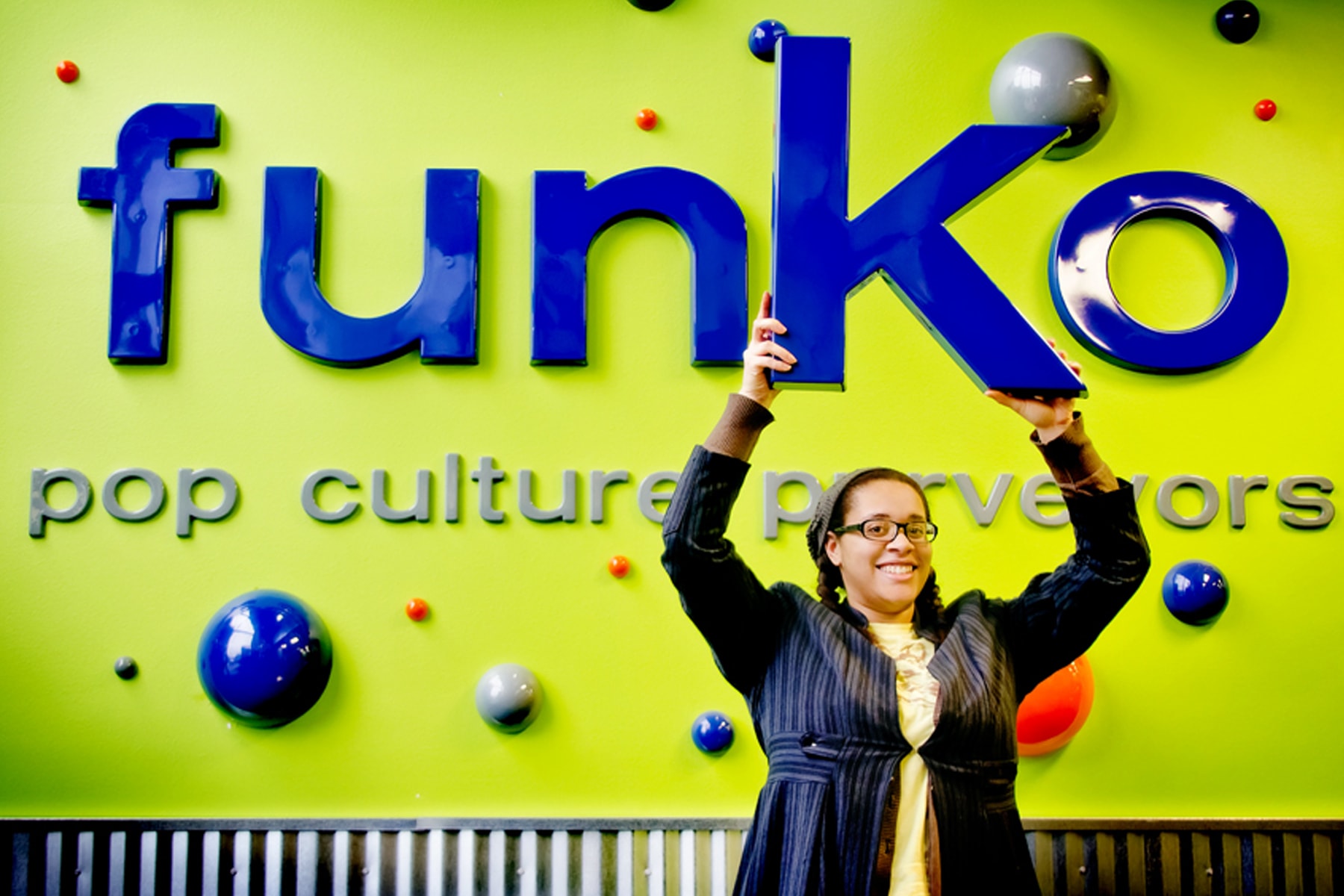 Nnenna Ijiomah smiling and holding the K from the Funko logo over her head at the company's office in Everett, Washington