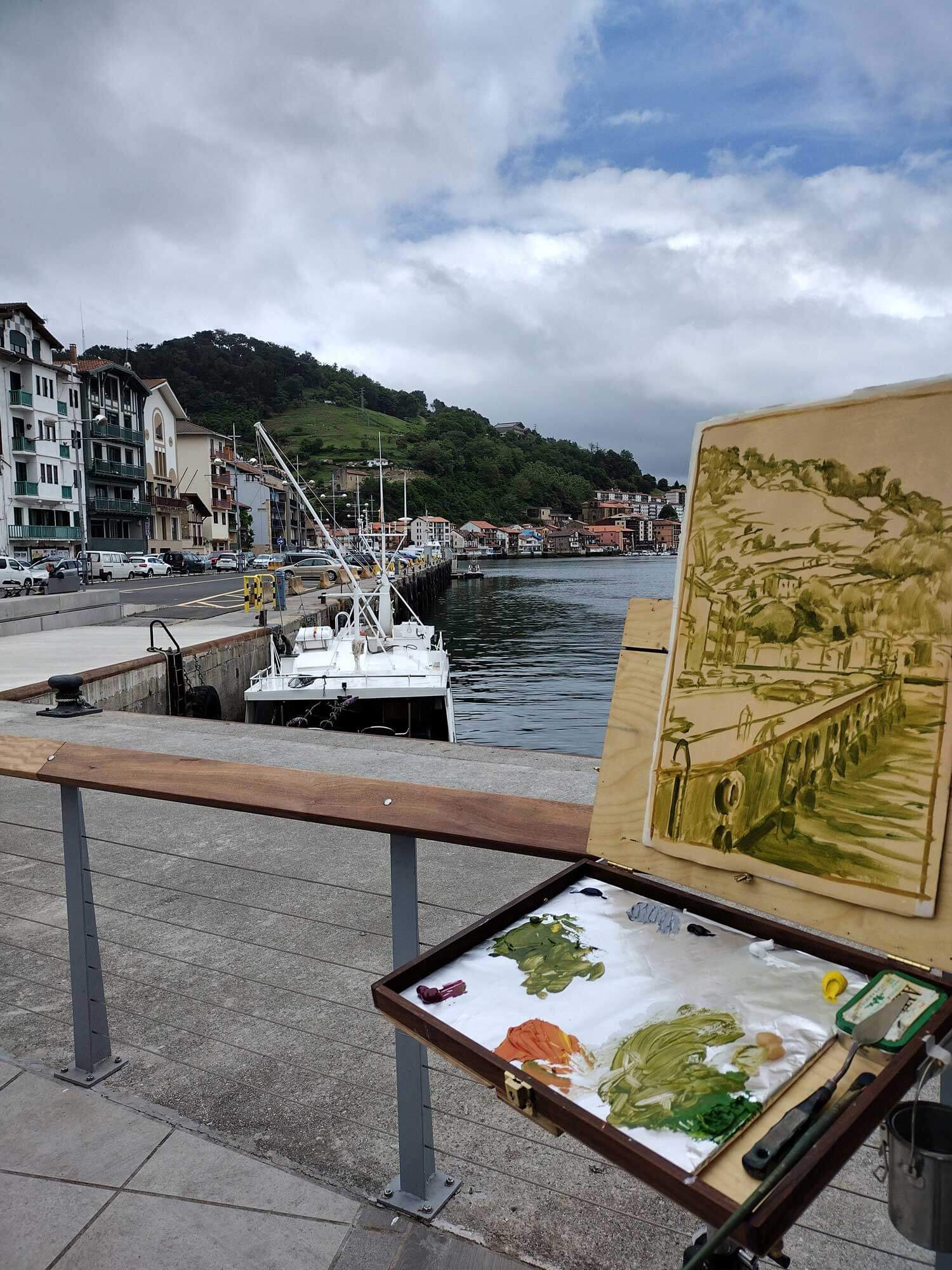 An unfinished painting looks over a harbor with a boat in the water and buildings to the side.