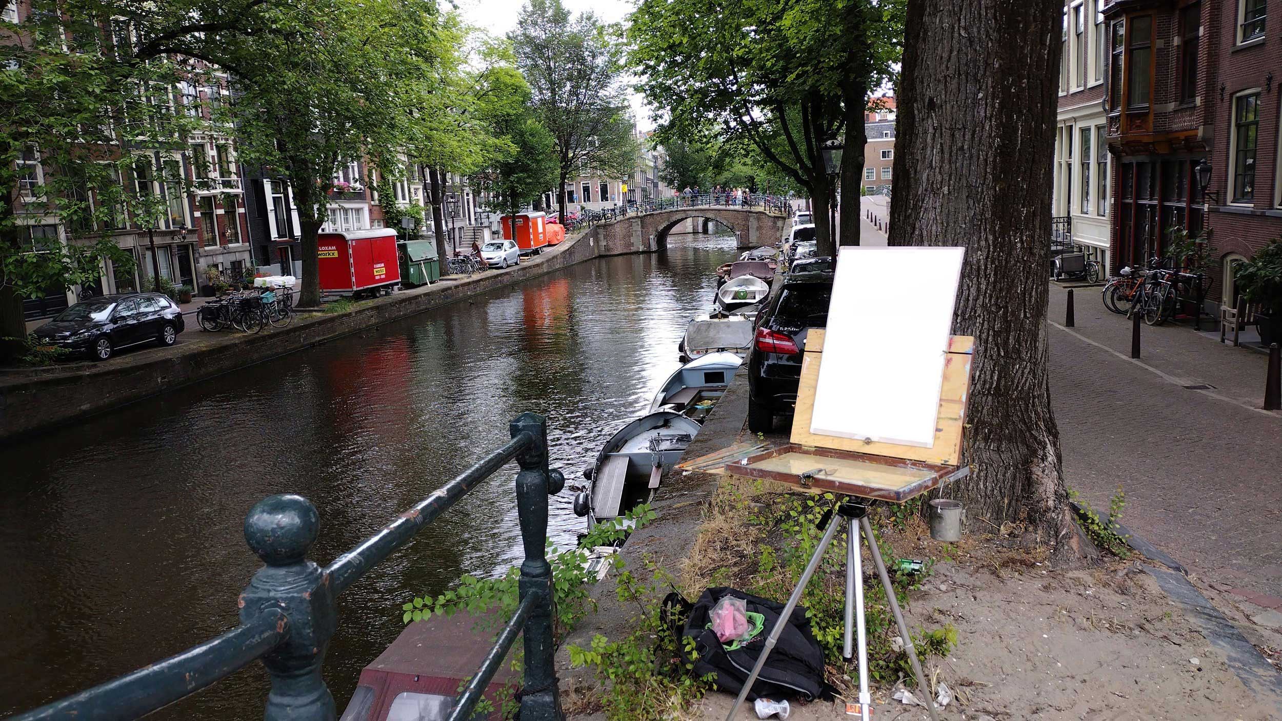 A canvas is set up on an easel on the edge of a canal in Amsterdam.