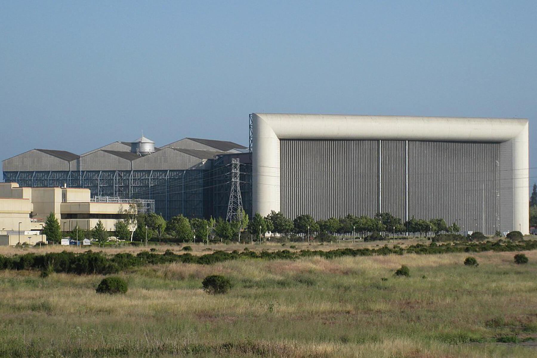 An exterior view of a very large grey wind tunnel building with fields in the foreground.