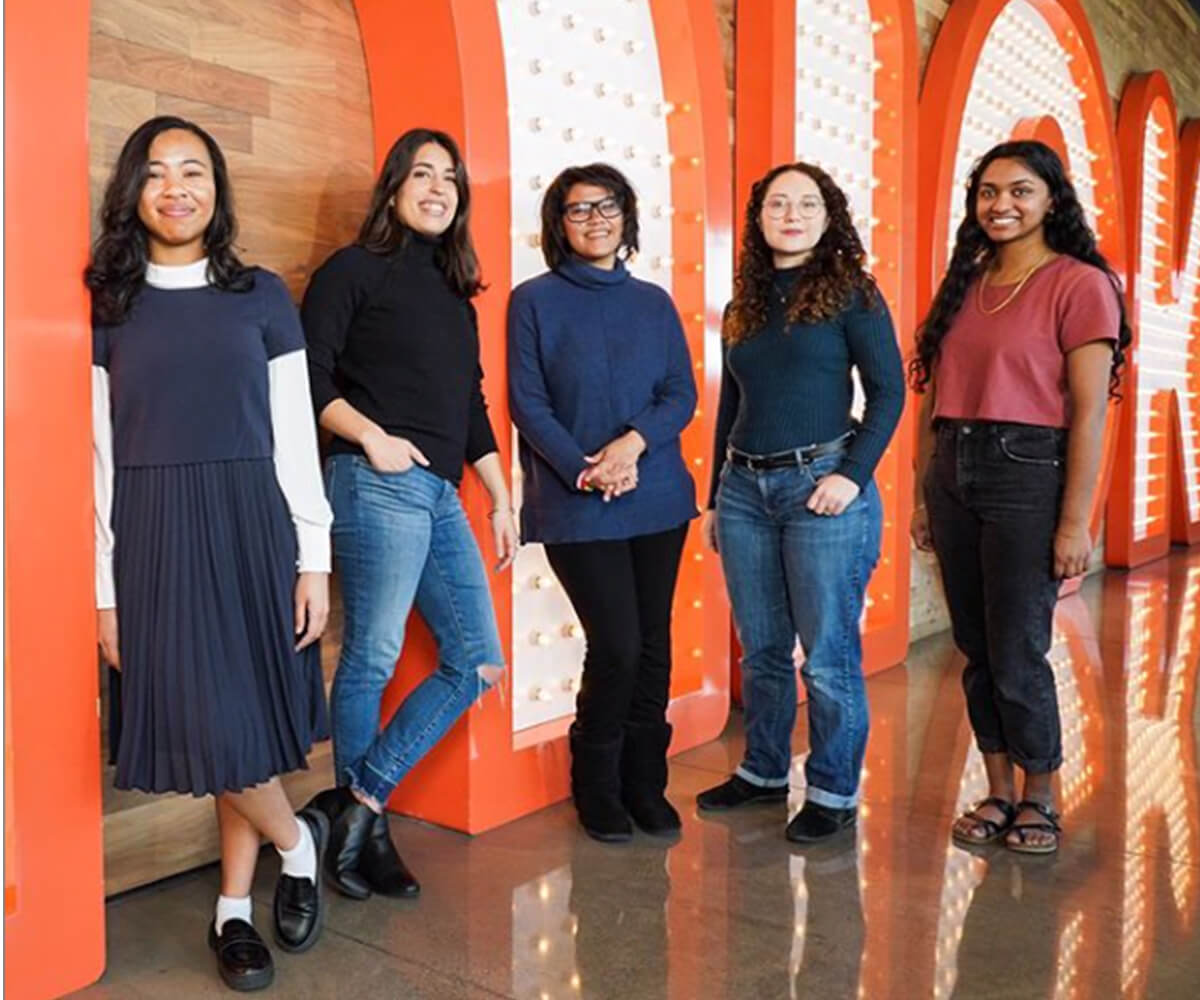 Shannon Parayil poses in front of a large, orange Nick sign with the other 2020 Nick Artist Program winners.