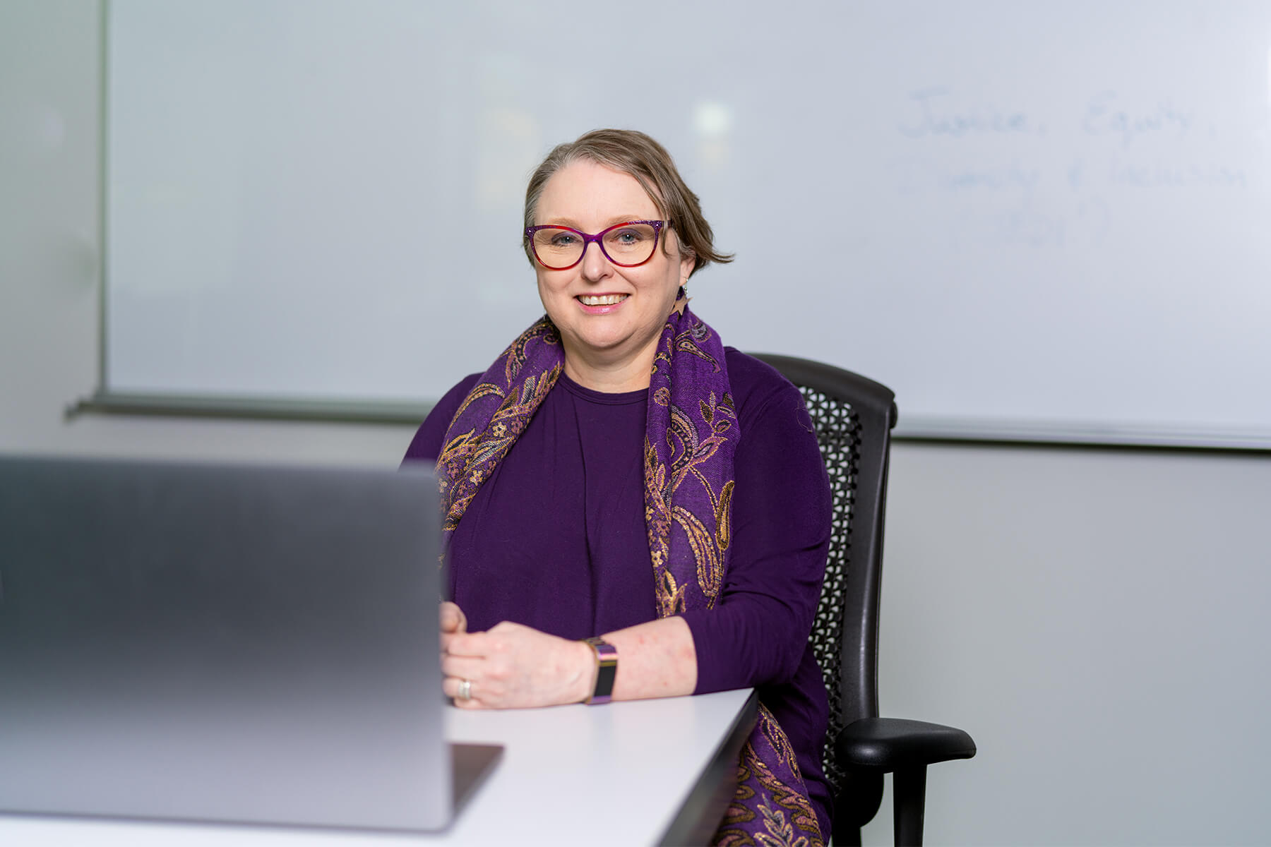 Senior lecturer Sonia Michaels sits in front of a classroom white board.