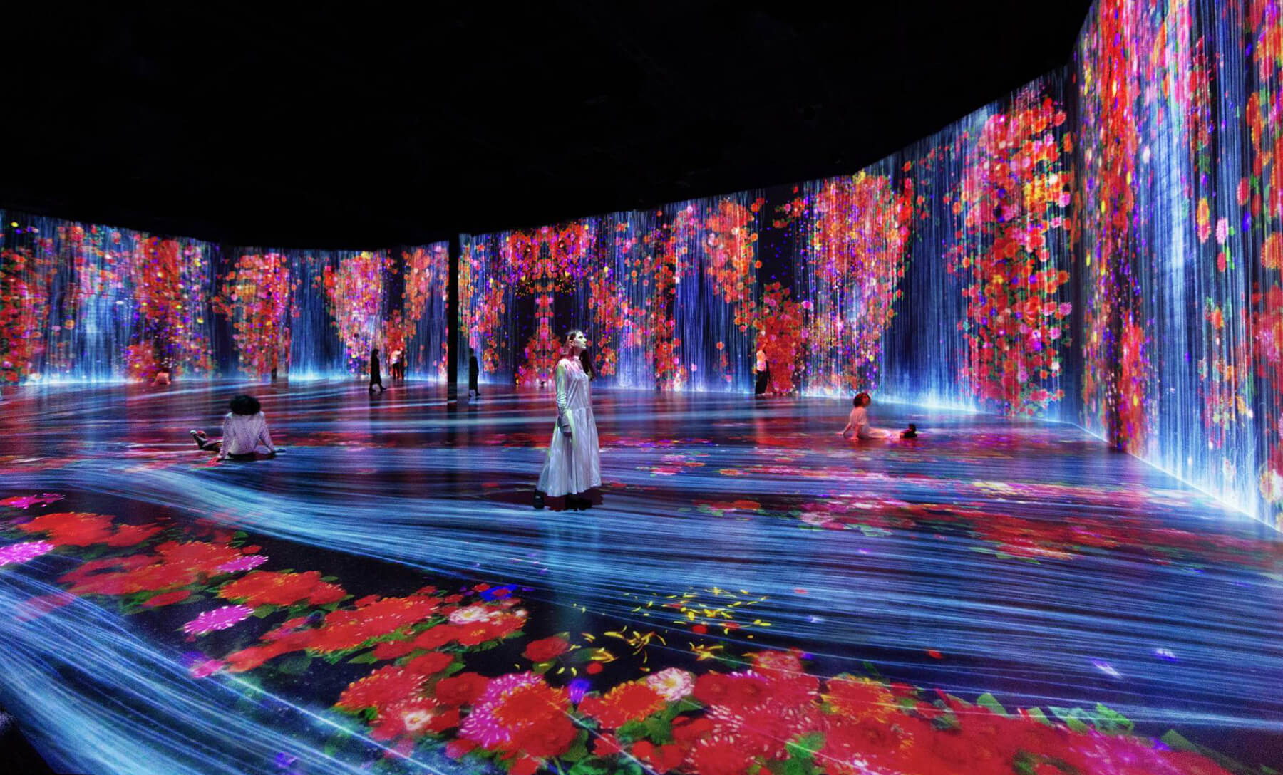 Viewers look at an enormous room full of digital flowers and water.