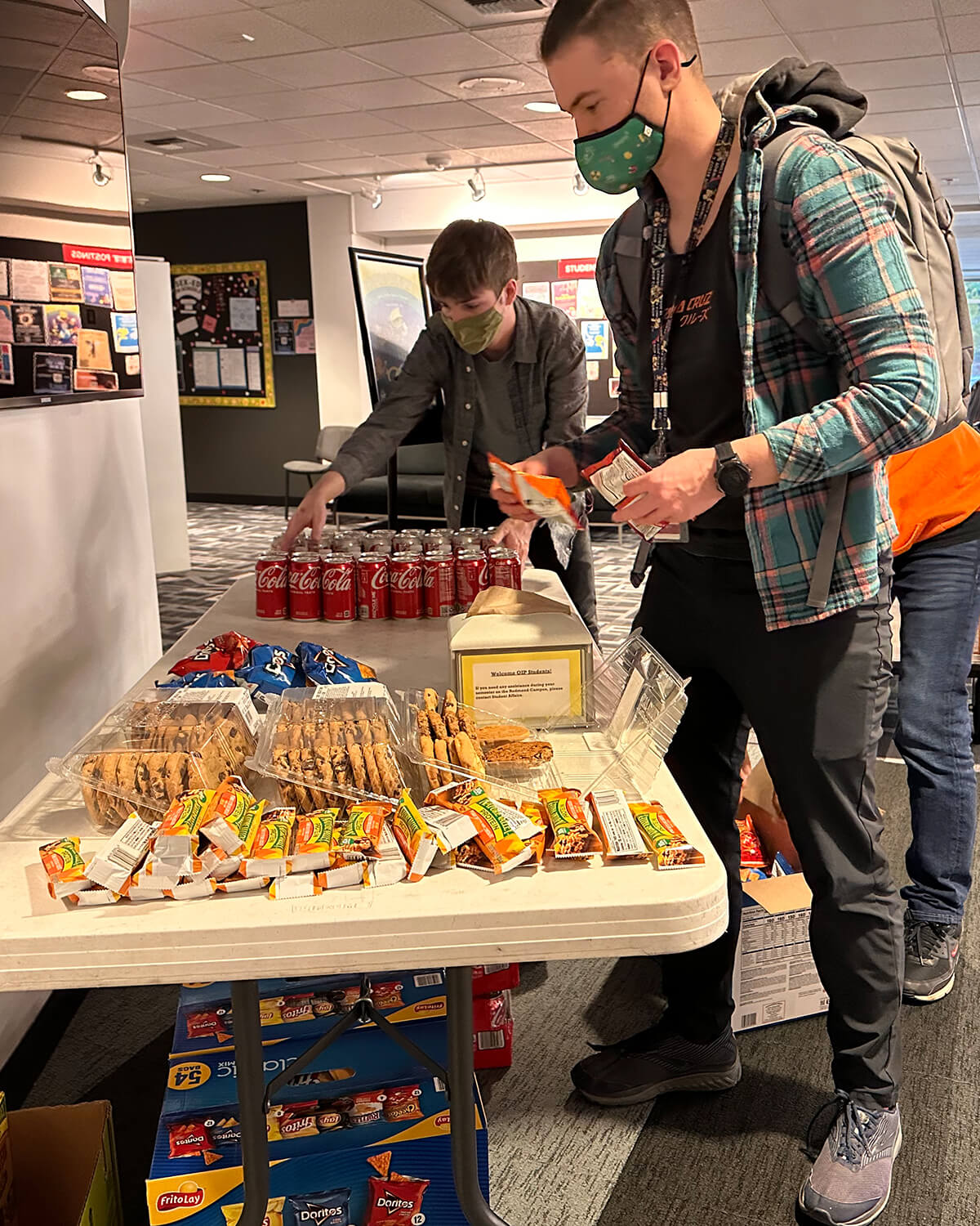 DigiPen student Li Baum places snacks on a table full of cookies, granola bars, chips, and soda.