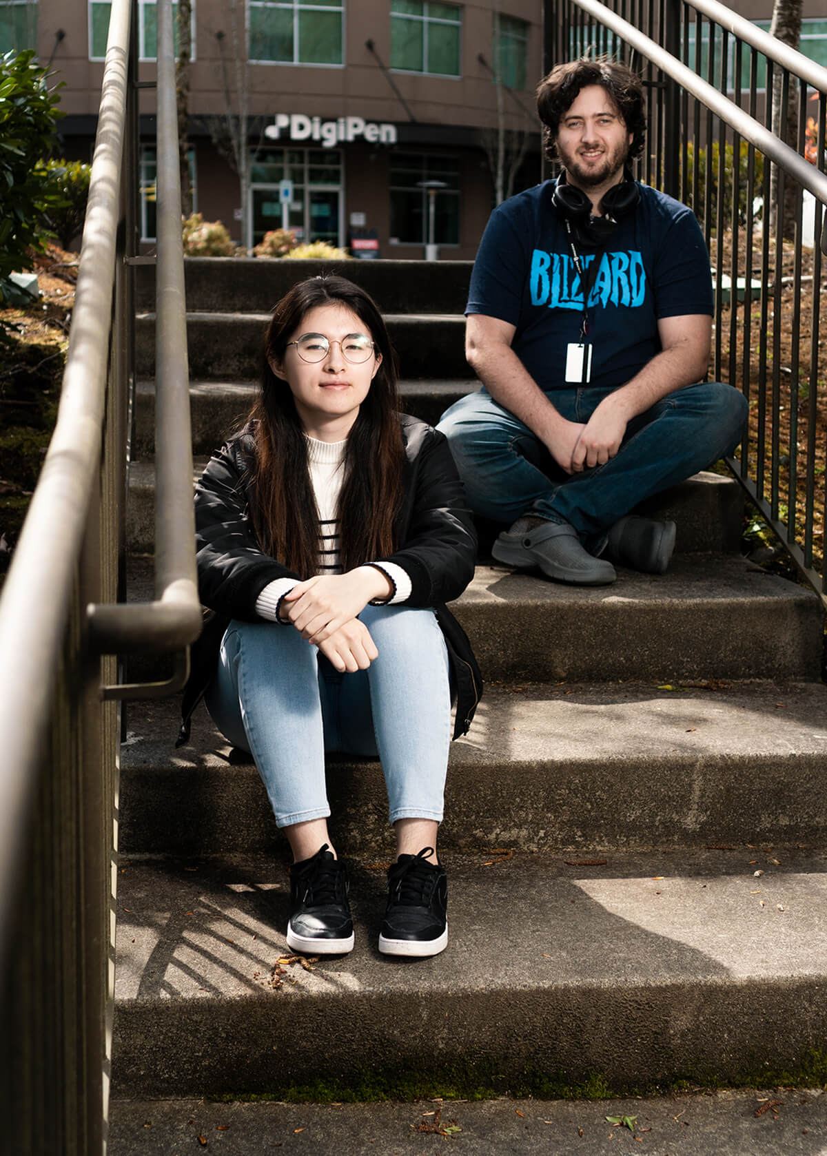 Students Joe Rouverol and Annie Hanson sit on concrete steps in front of DigiPen’s main building.