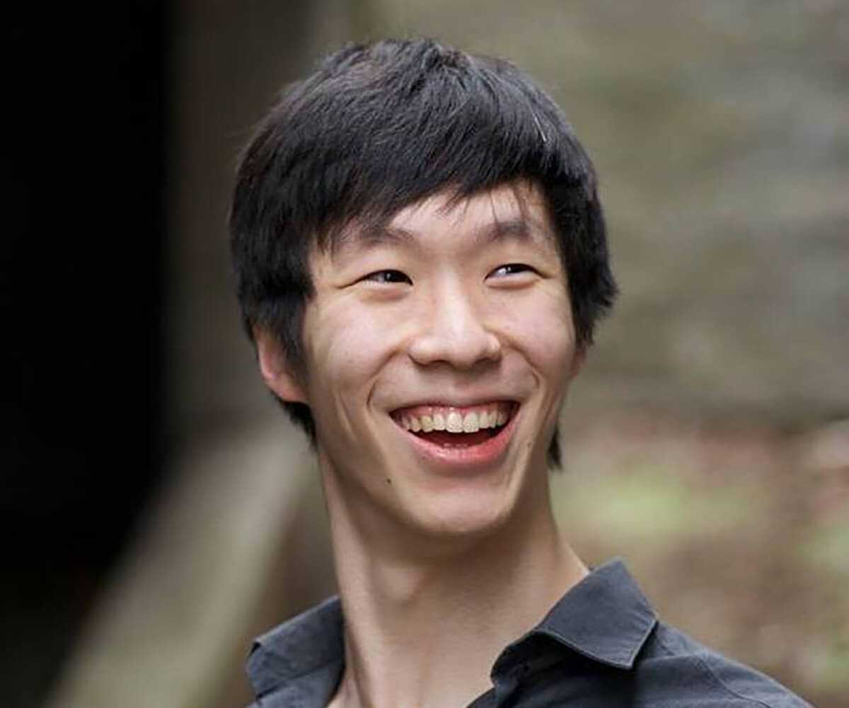 Head shot of a man with black hair in a black collared shirt smiling and looking off toward the right.