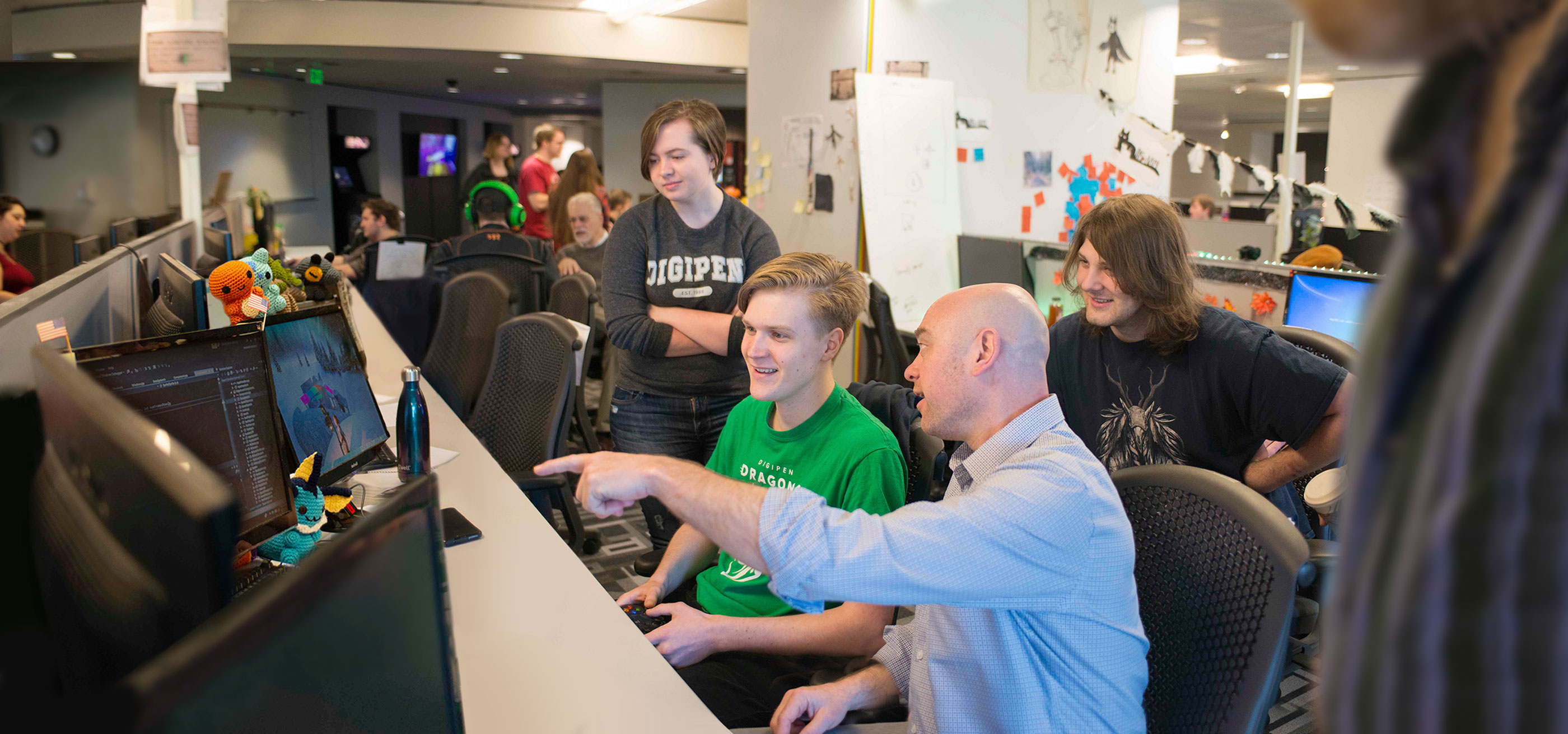 Students and an instructor sit at a desk playing a computer game.