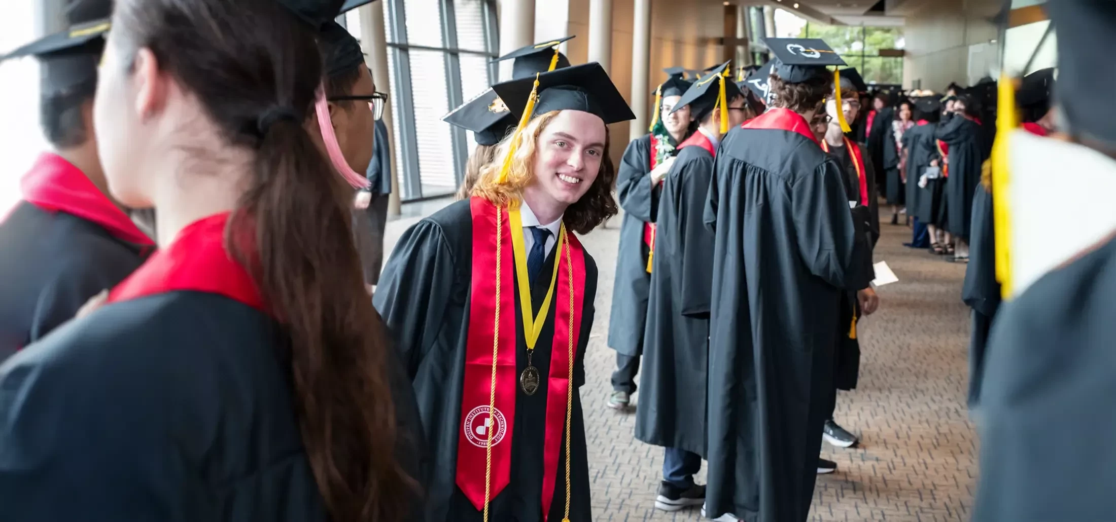 DigiPen student in graduation robes peeks around his graduating peers.