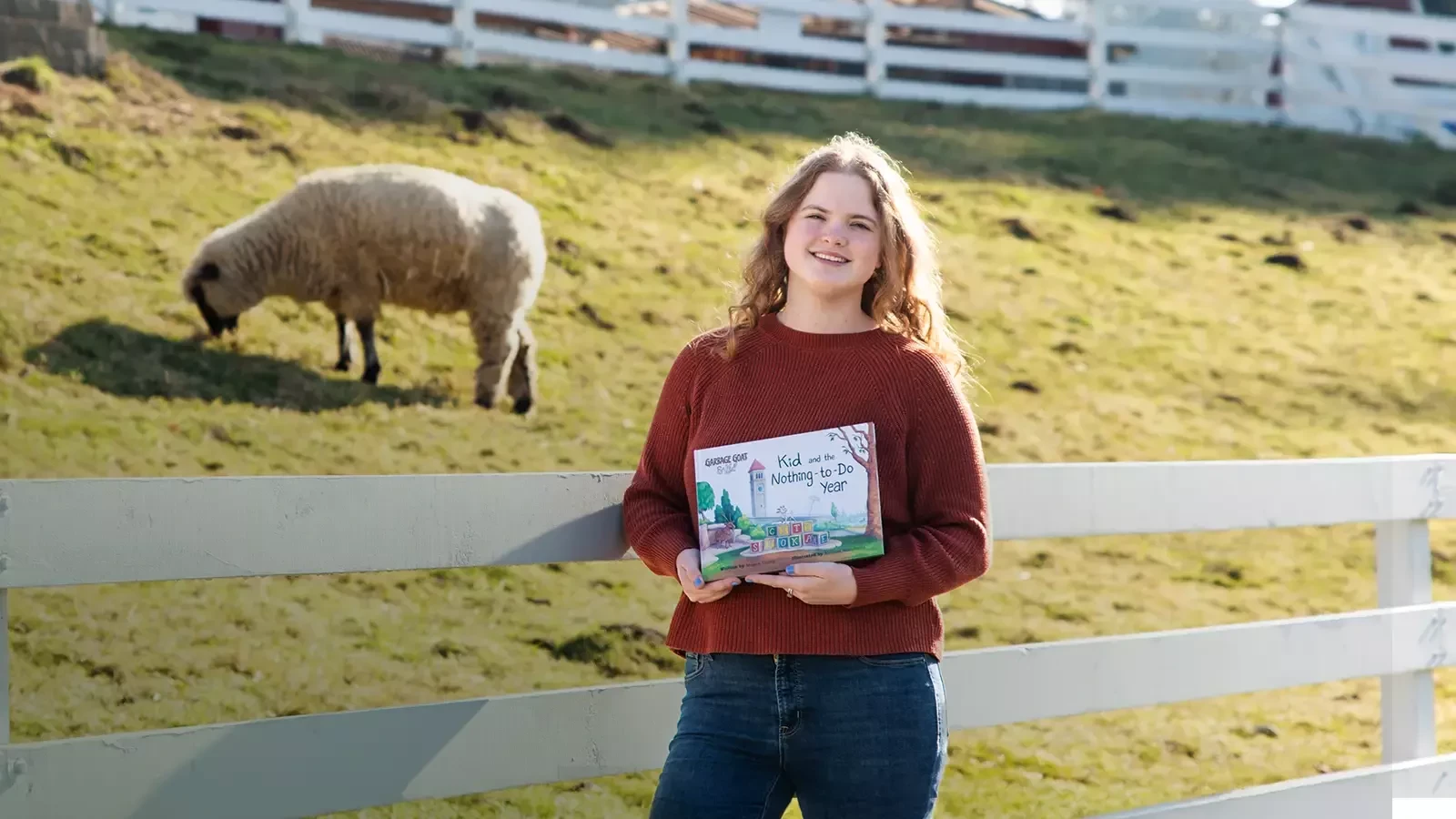 Melissa holds her book near a single sheep.