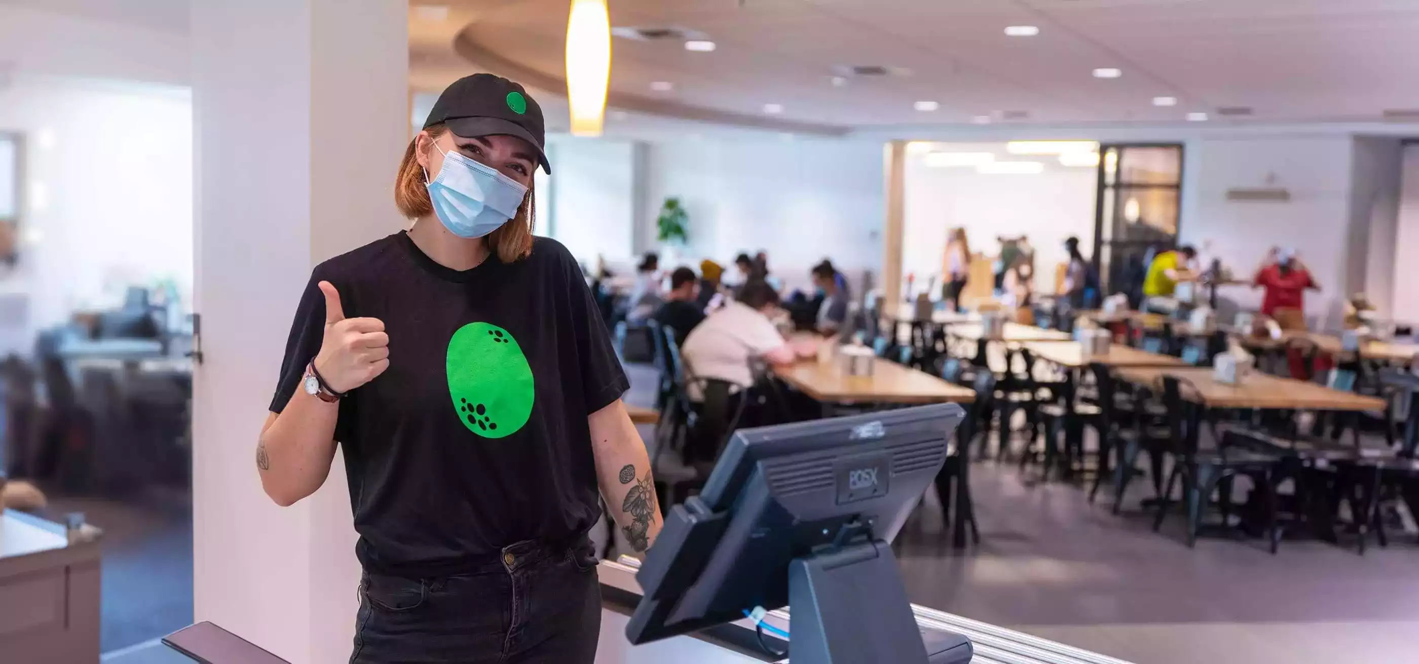 A DigiPen student working the cafe's cash register gives a thumbs up.