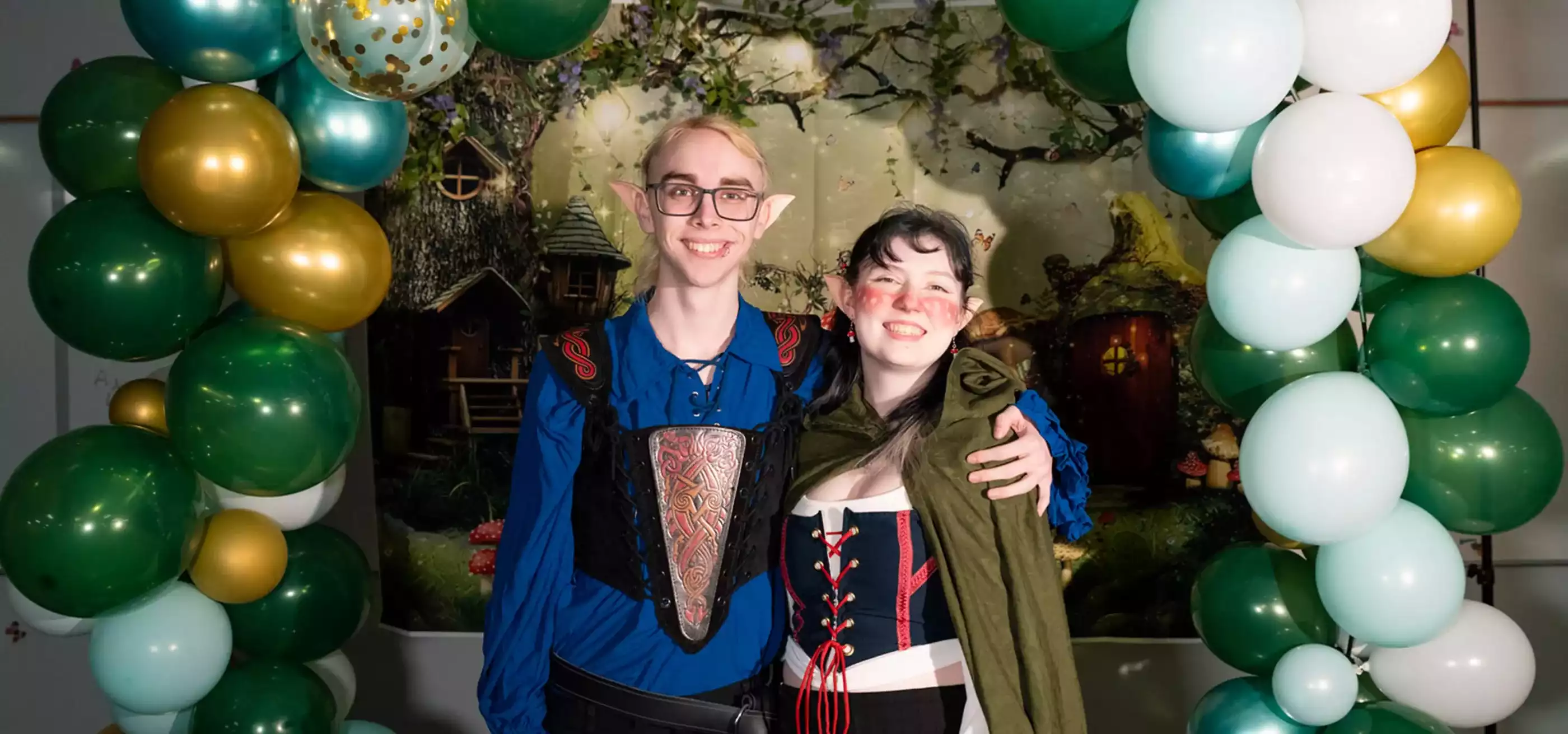Two DigiPen students dressed as elves pose in front of a balloon arch at the first annual DigiProm.