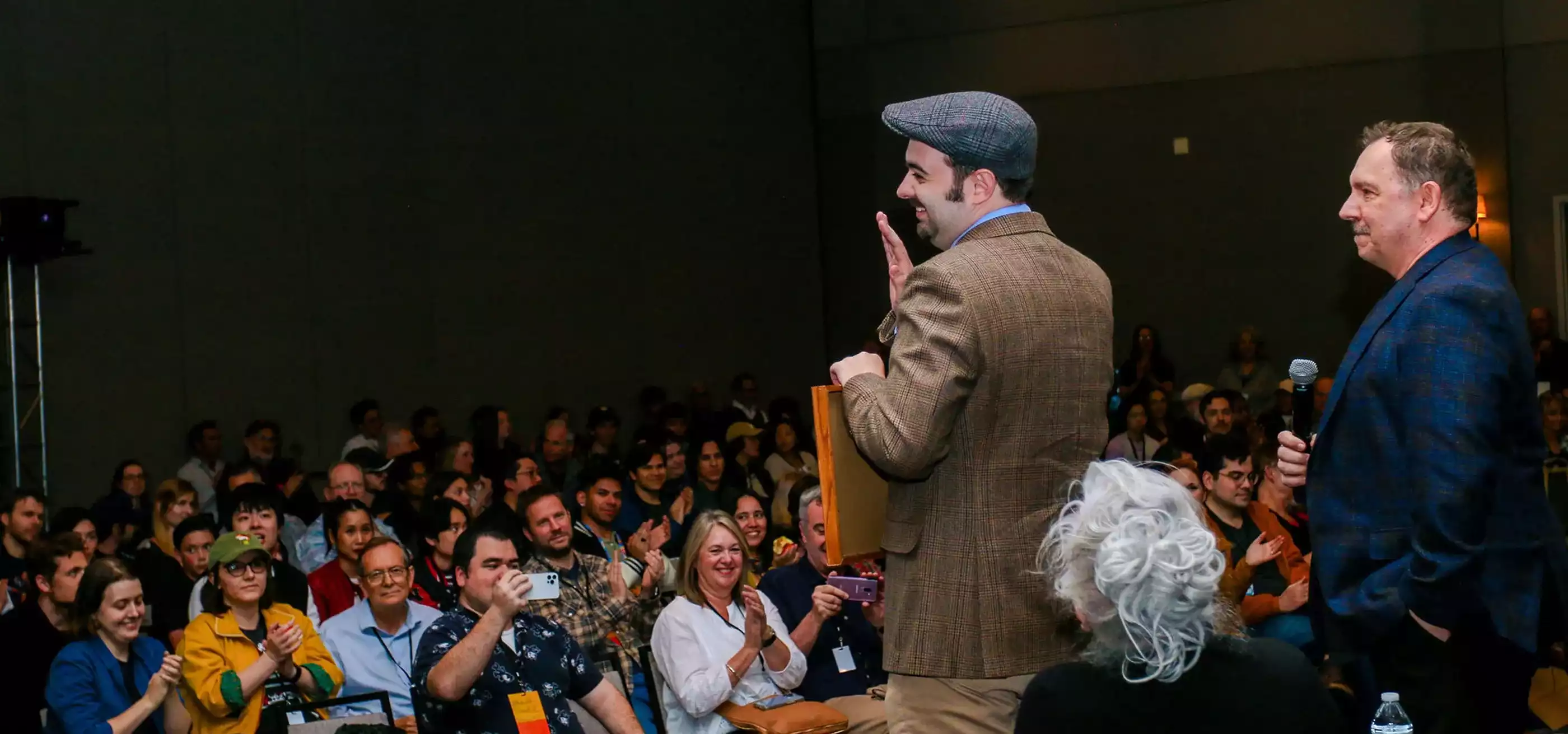 Edward Davies stands by Andreas Deja on stage at the CTN Expo and waves to an applauding crowd holding his award certificate.
