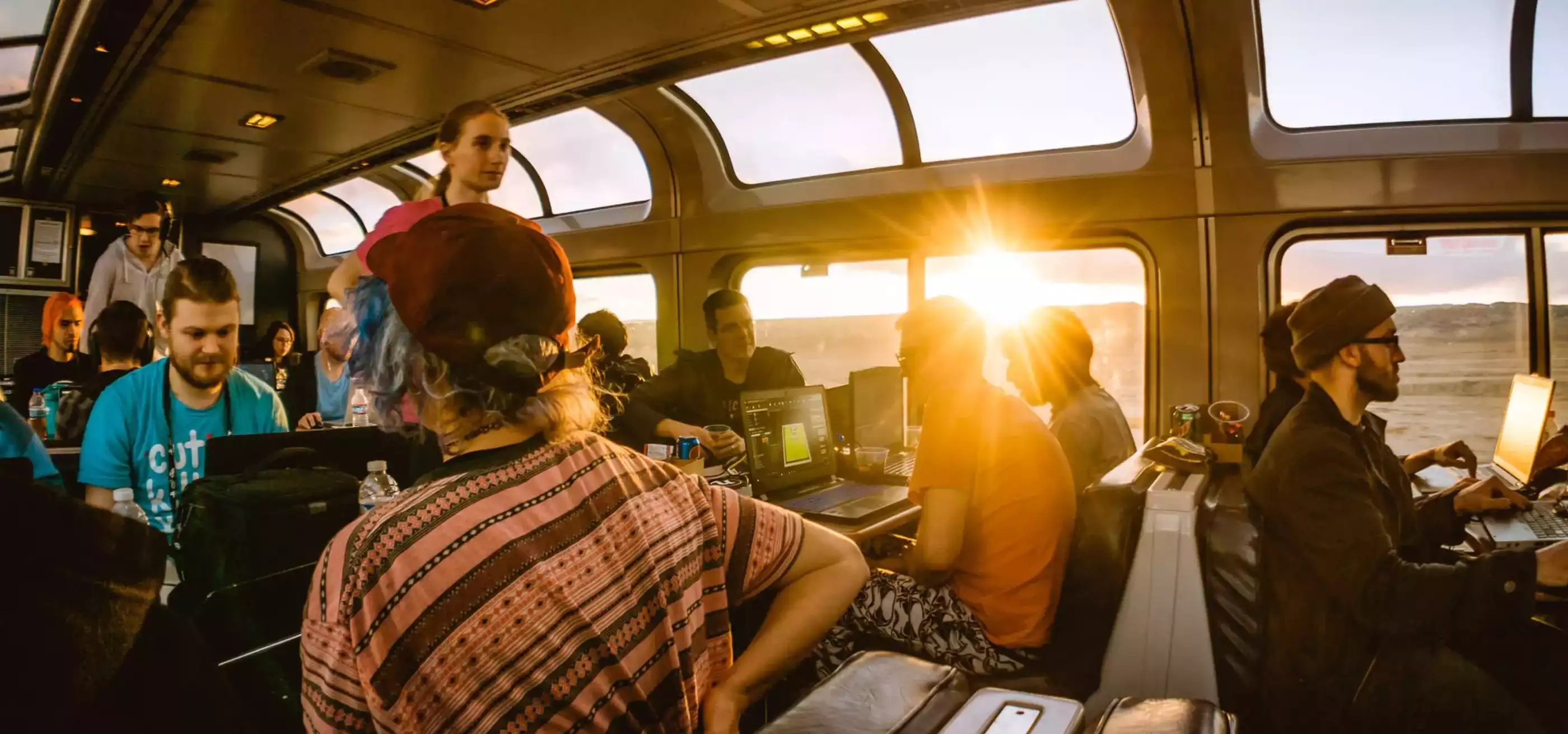 Afternoon sun beaming through the windows of the train's observation car where gamers collaborate on their laptops